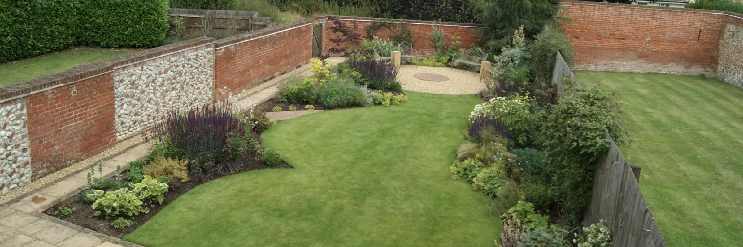 A walled garden with a sweeping curved lawn and deeply planted borders